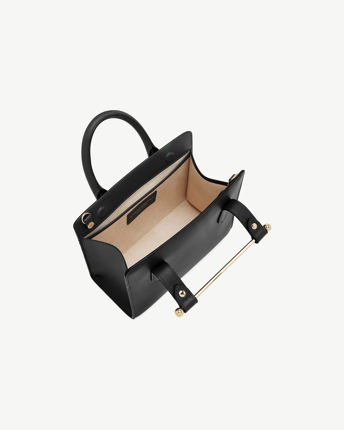 Black mini tote bag open, beige interior, top handles and gold metal bar.