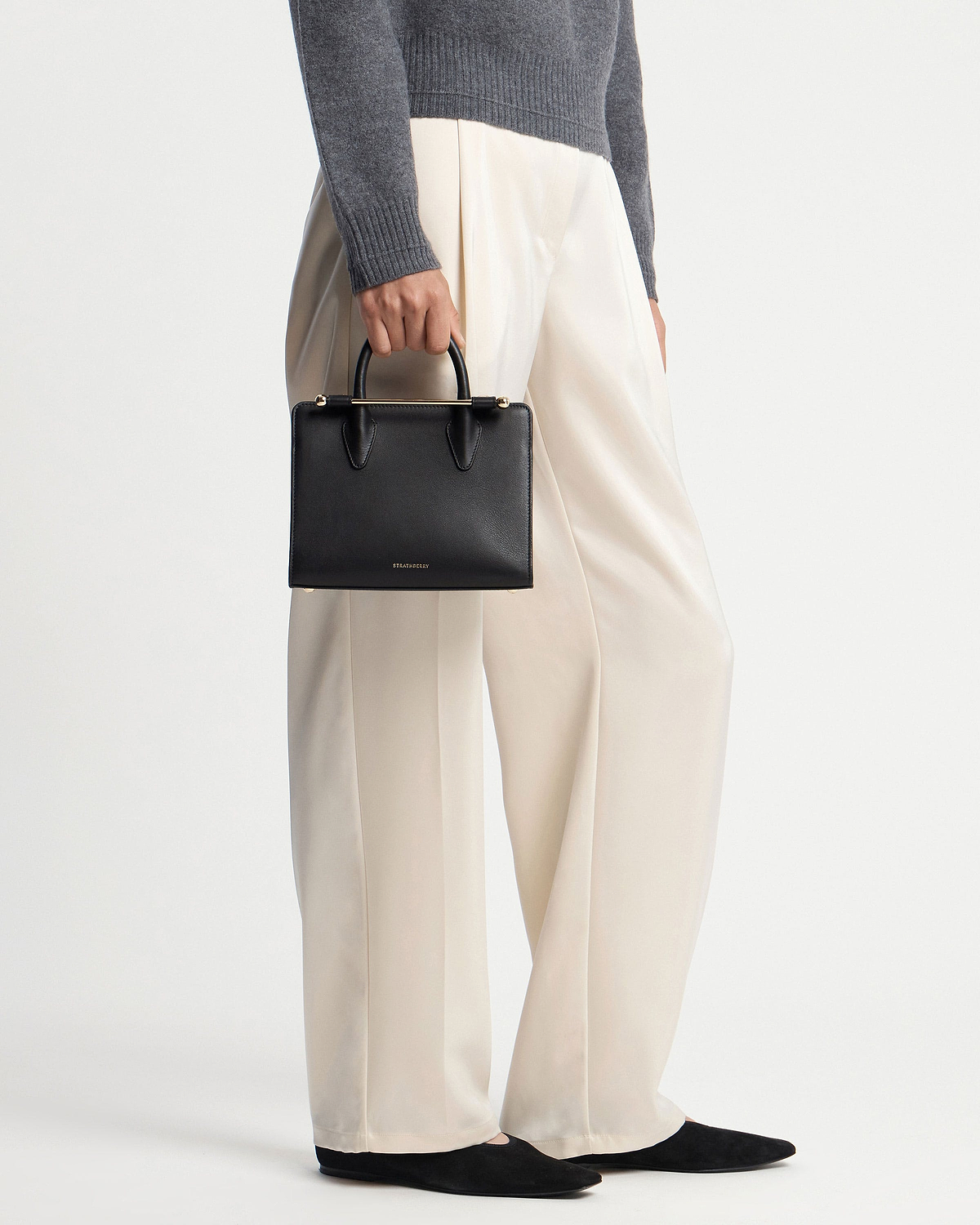 Model holding black Strathberry mini tote with top handles and gold bar hardware.