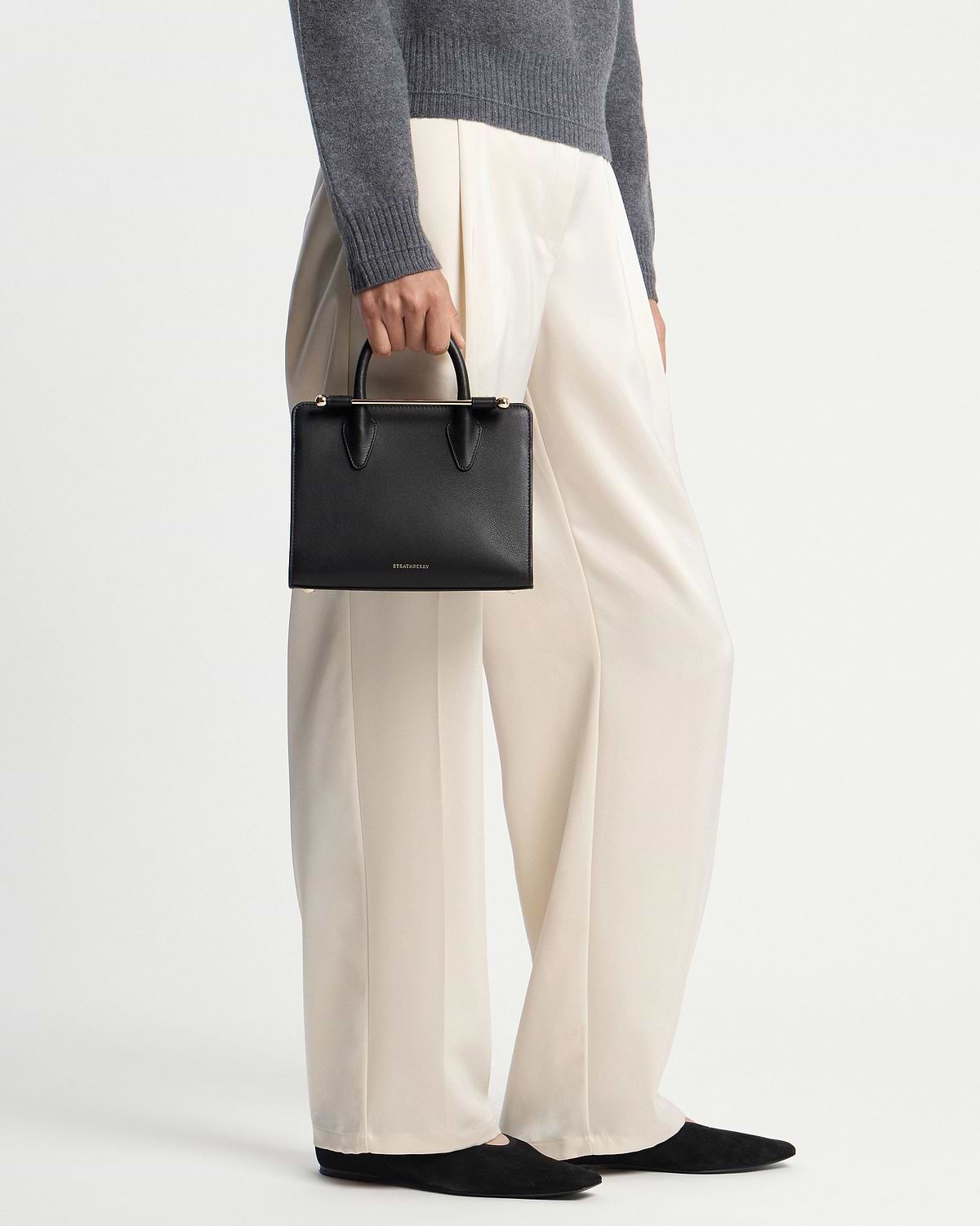 Model holding black Strathberry mini tote with top handles and gold bar hardware.