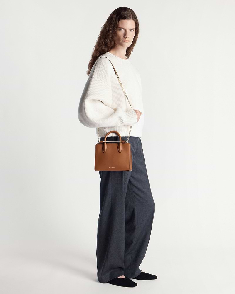 Model wearing white jumper carrying a chestnut mini tote with chain strap.