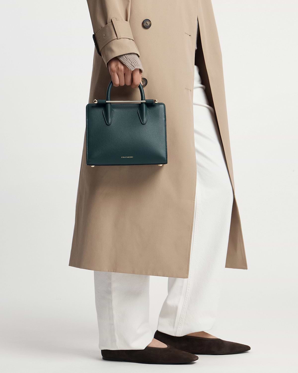 Strathberry bottle green mini tote held by model wearing beige trench and white trousers.