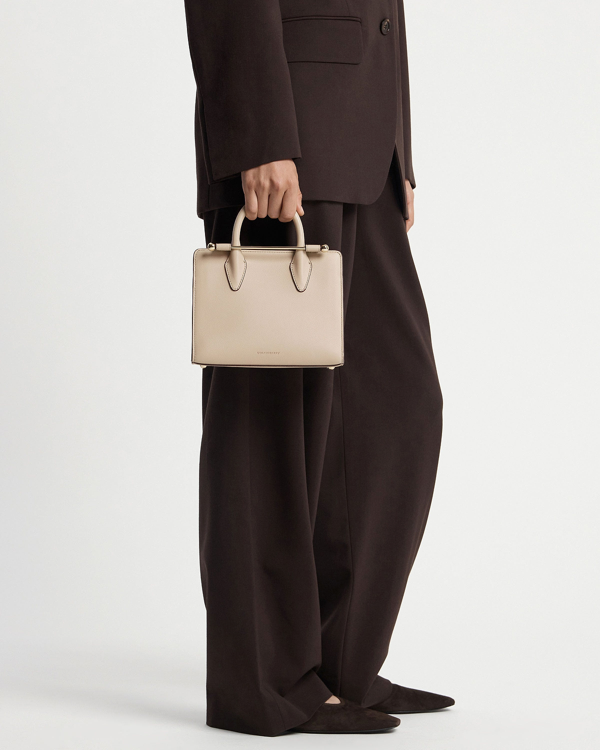 Model cropped below waist holding oat Strathberry mini tote with top handles.
