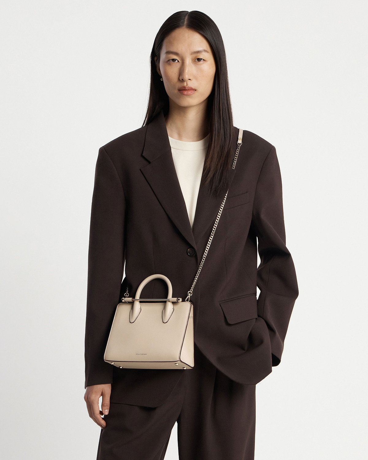 Model wearing Strathberry oat mini tote with top handles and gold chain strap.