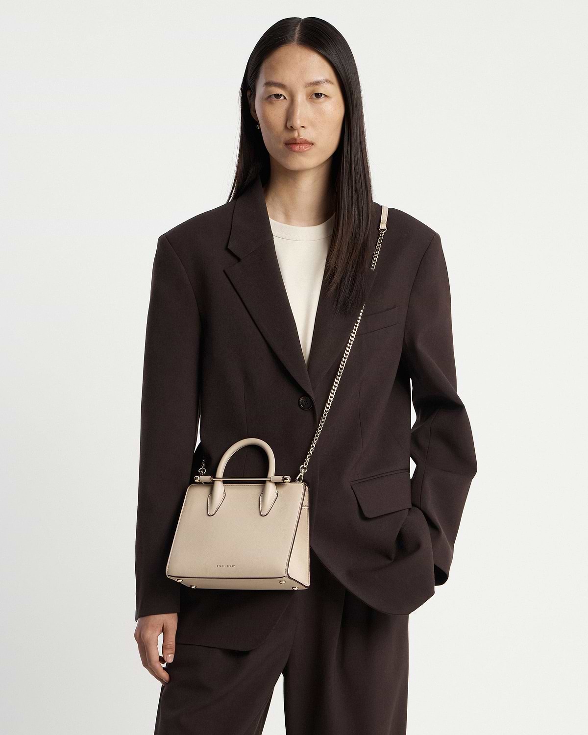 Model wearing Strathberry oat mini tote with top handles and gold chain strap.