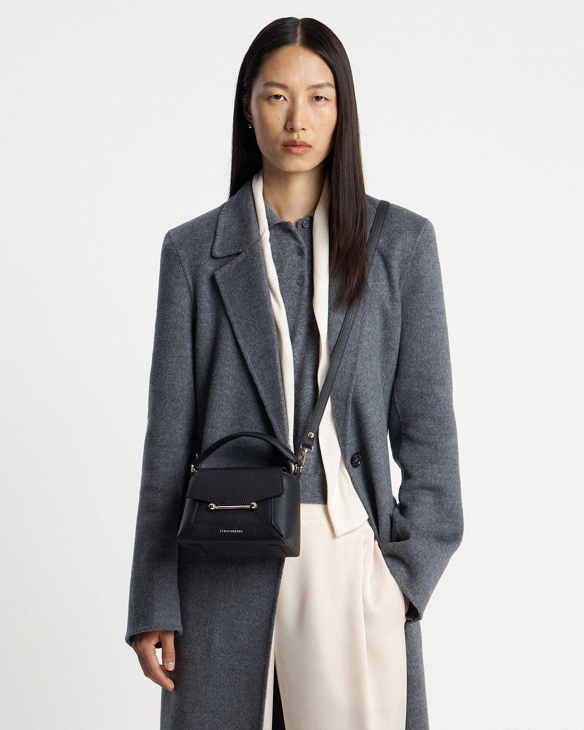 Model wearing a Strathberry Mosaic Nano black leather bag worn crossbody with grey coat