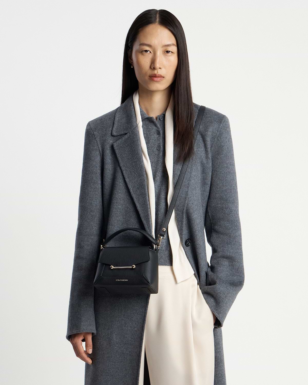 Model wearing a Strathberry Mosaic Nano black leather bag worn crossbody with grey coat