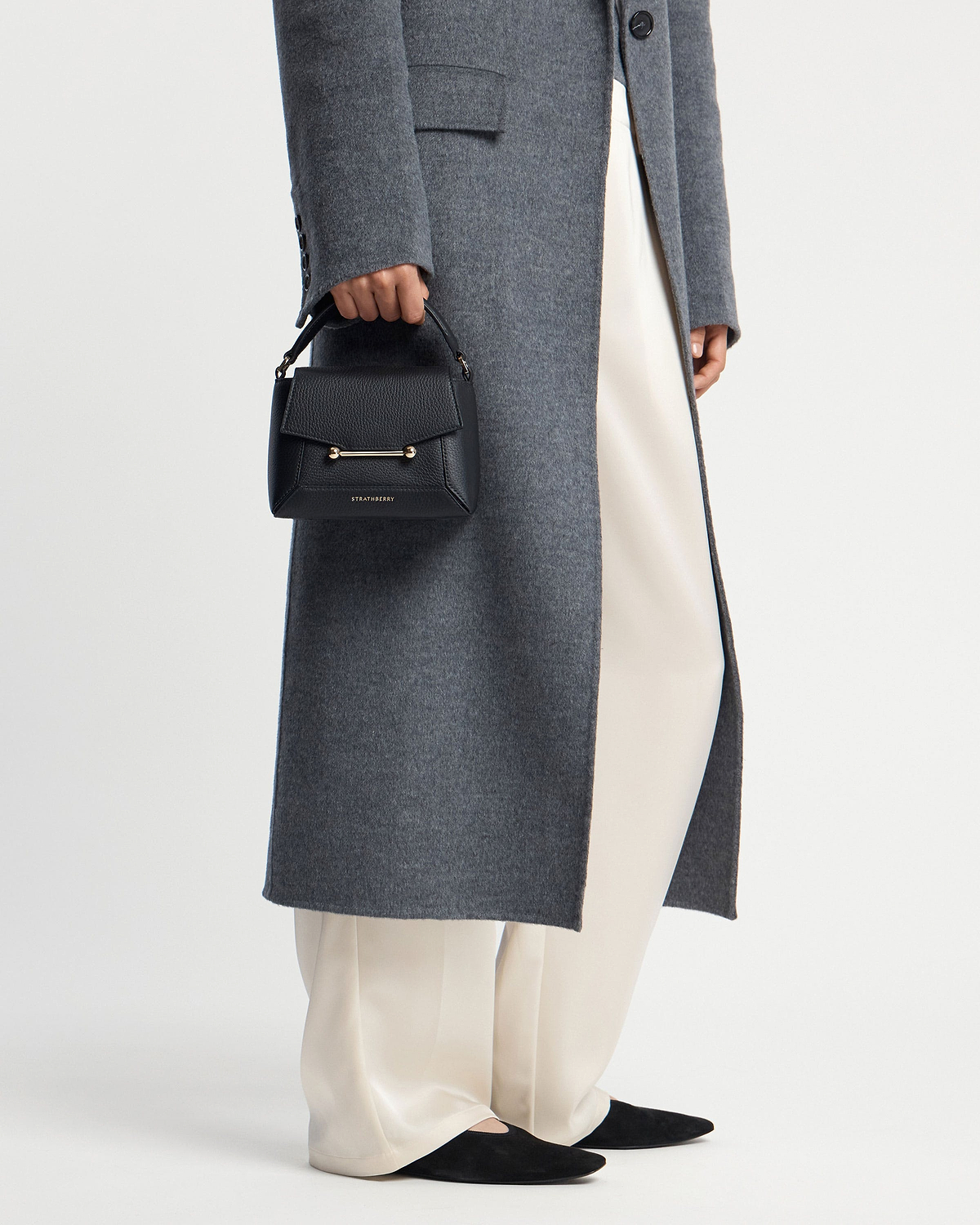 Model holding black Strathberry mini top-handle bag with gold bar detail.