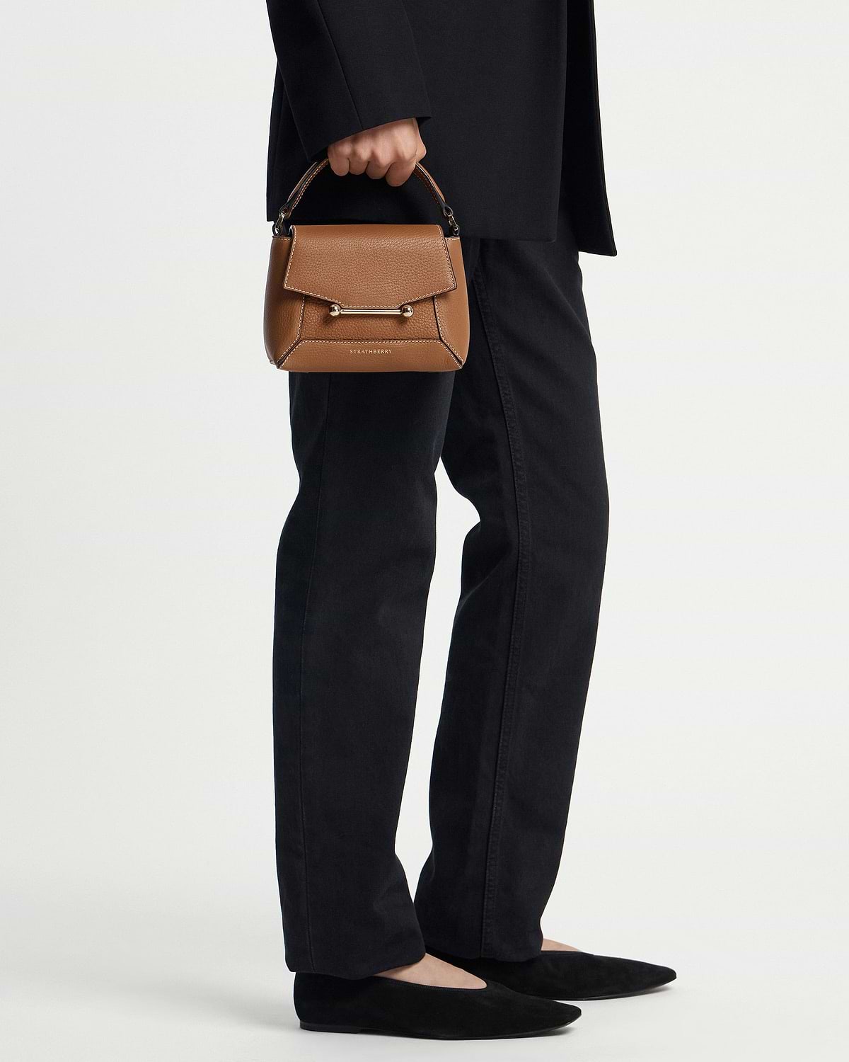 Tan Strathberry Mosaic Nano handbag with vanilla stitching held by model wearing black trousers.