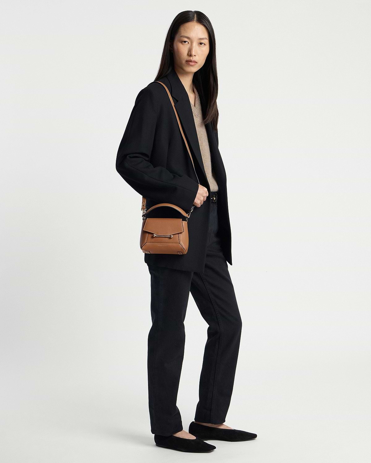 Woman wearing a black outfit carrying a tan top-handle crossbody bag with vanilla stitching.
