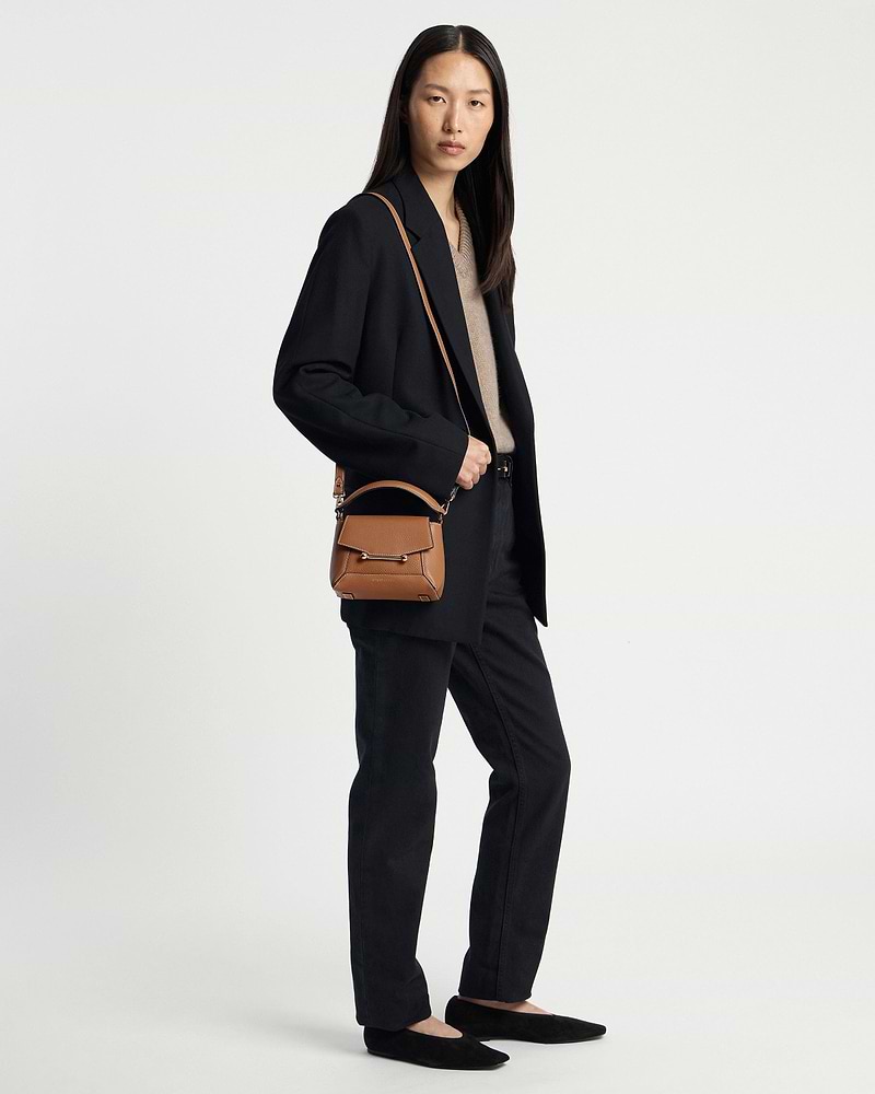 Woman wearing a black outfit carrying a tan top-handle crossbody bag with vanilla stitching.