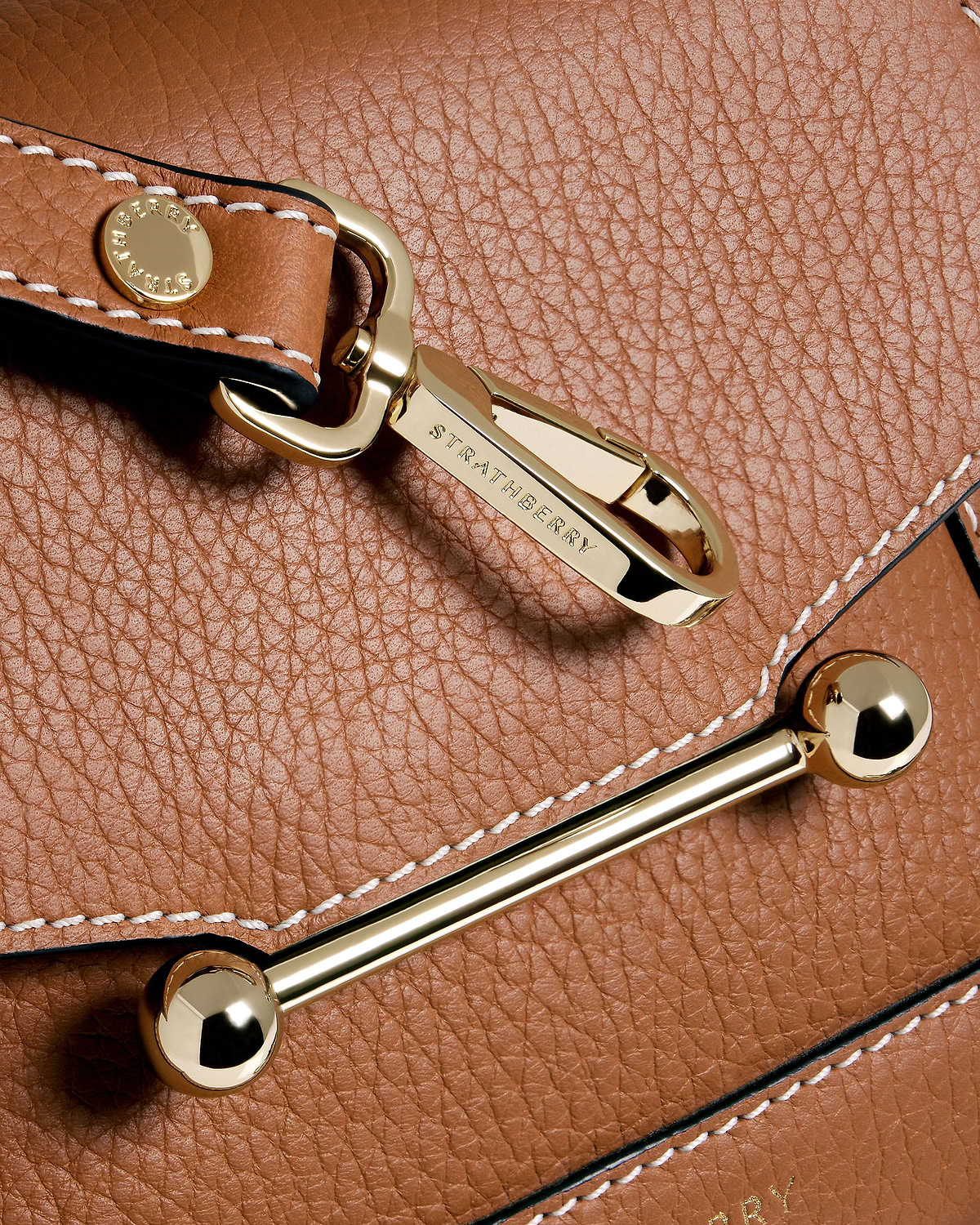Gold Strathberry clasp on tan pebbled leather with vanilla stitching.