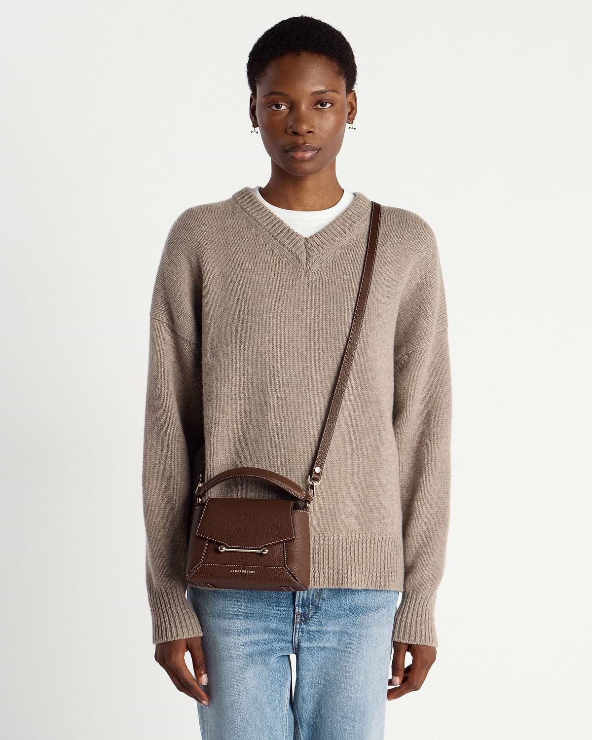 Model wearing chocolate brown leather mini bag with vanilla contrast stitching, top handle and strap.