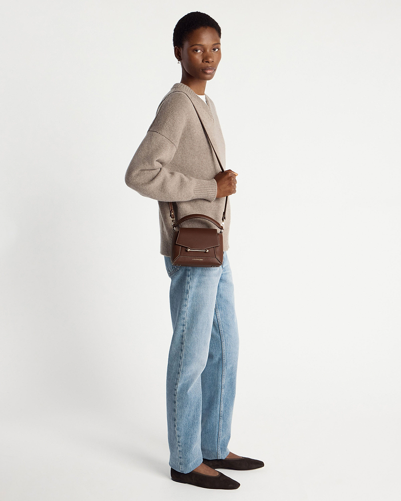 Model wearing a chocolate leather mini top-handle bag with vanilla stitching and crossbody strap.