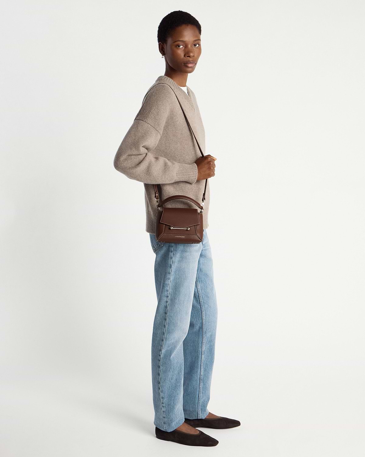 Model wearing a chocolate leather mini top-handle bag with vanilla stitching and crossbody strap.