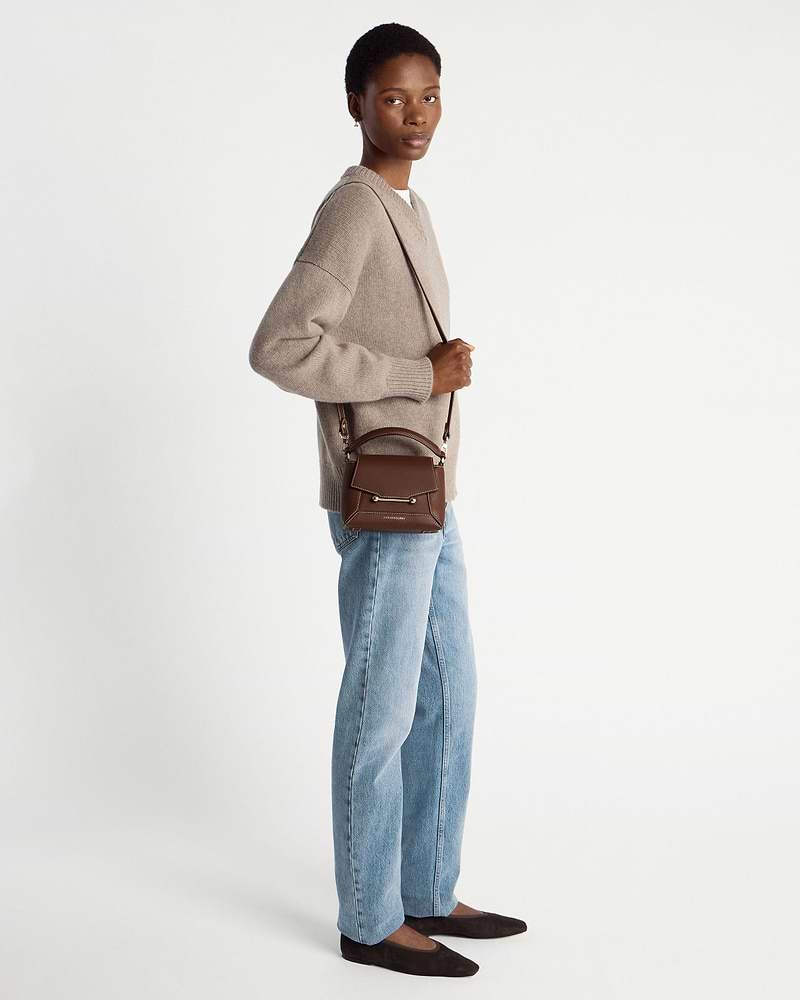 Model wearing a chocolate leather mini top-handle bag with vanilla stitching and crossbody strap.