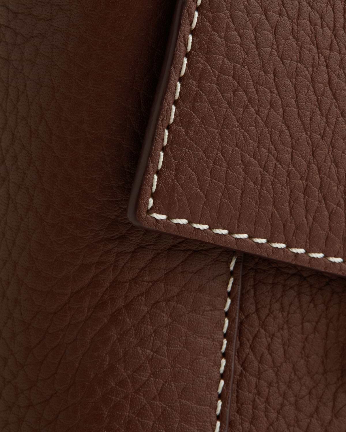 Chocolate brown pebbled leather with vanilla contrast stitching along a folded flap edge.