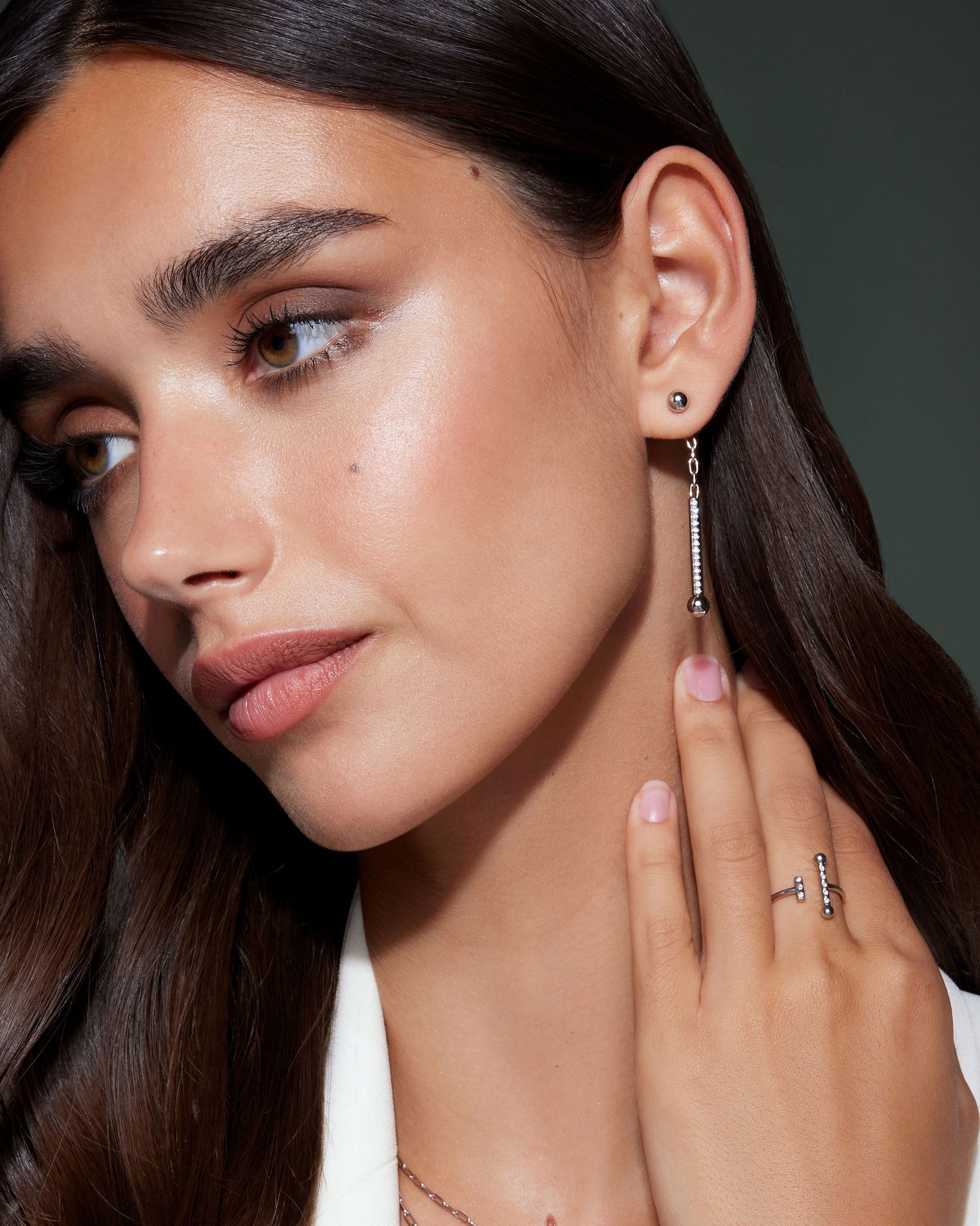 Woman wearing silver crystal music drop earrings and a matching ring, side portrait