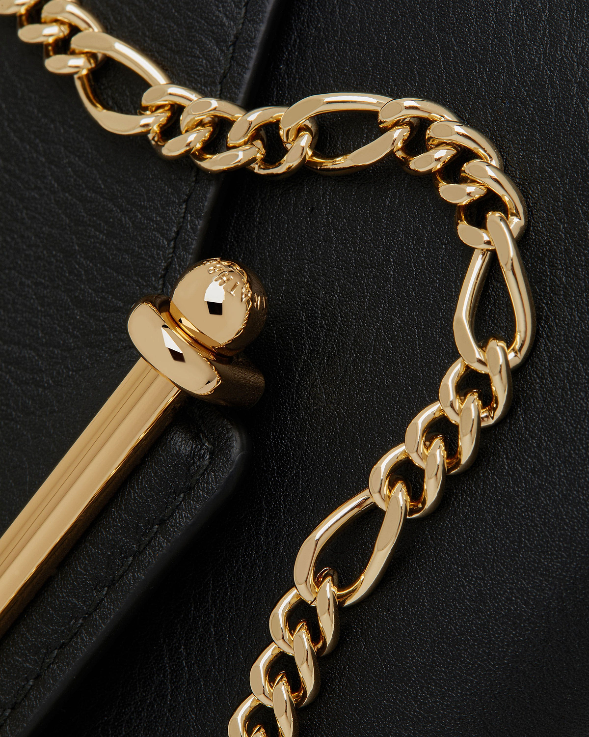 Gold chain and polished gold clasp on black grained leather wallet surface.