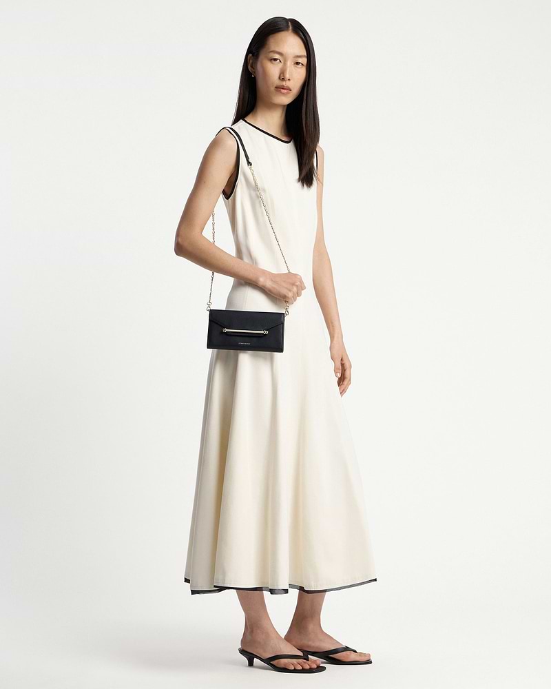 Model in cream sleeveless dress wearing a black chain wallet on a gold shoulder chain.