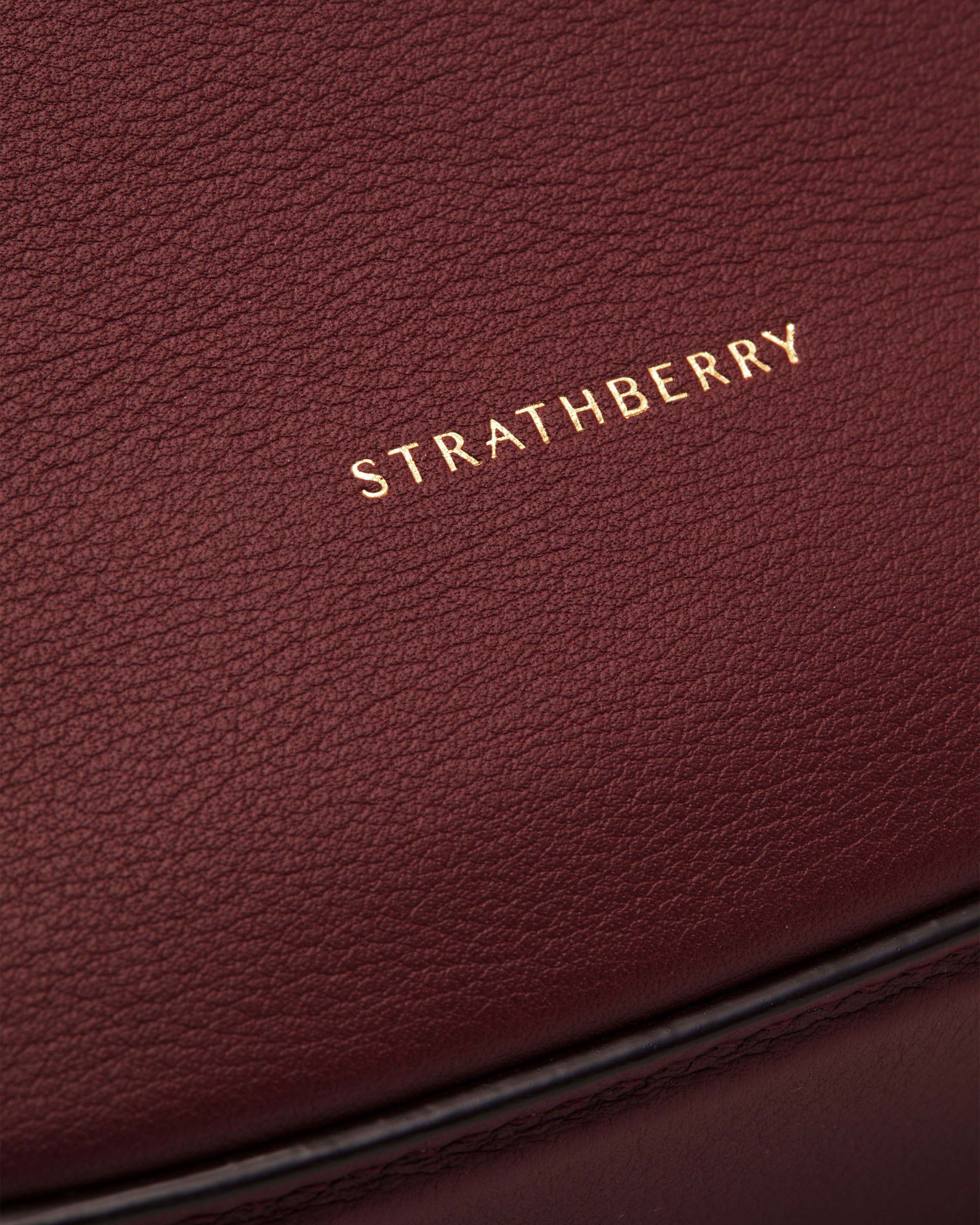 Strathberry logo stamped on oxblood leather crescent moon bag surface.