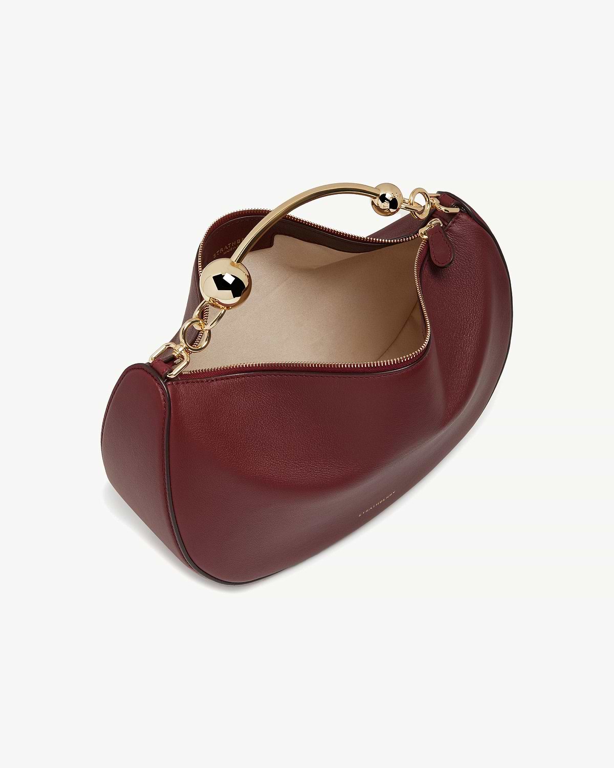 Oxblood leather crescent bag with gold curved top handle and beige interior.