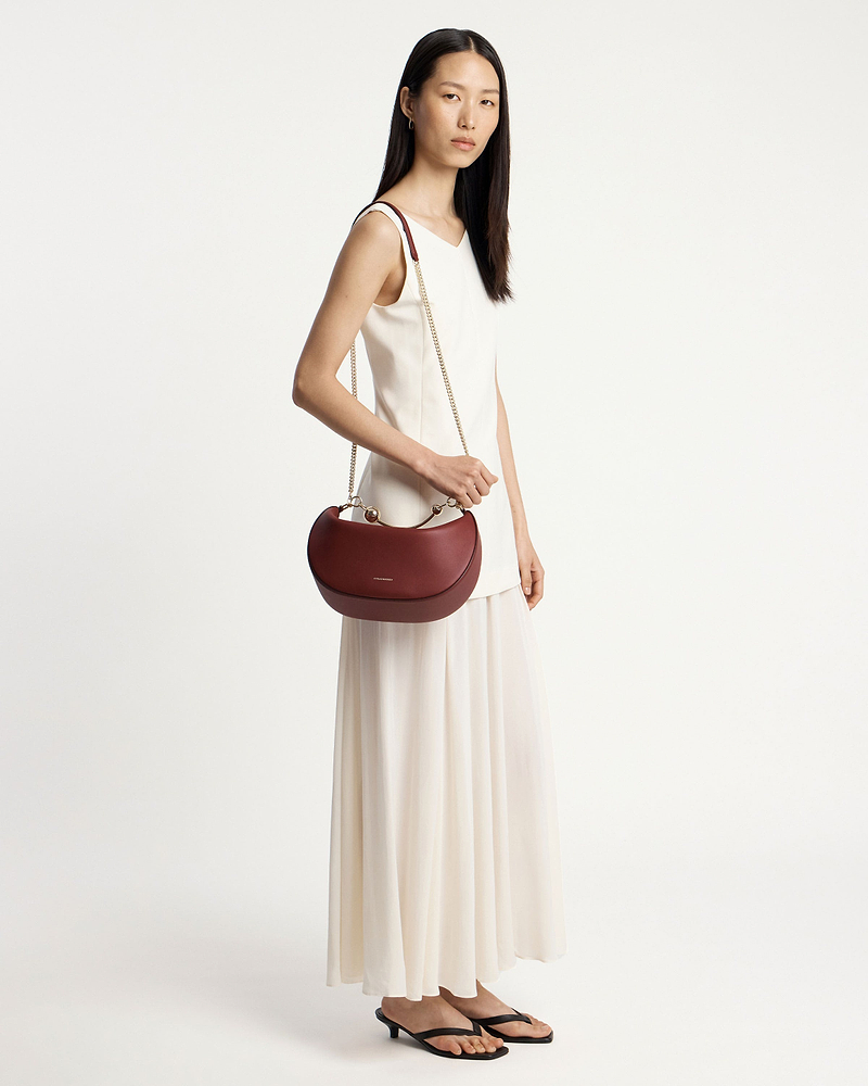 Woman in white dress carrying oxblood crescent moon bag with chain strap