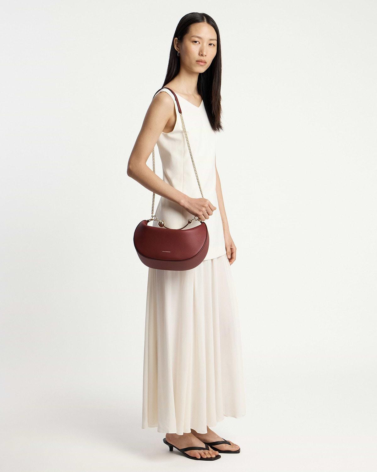Woman in white dress carrying oxblood crescent moon bag with chain strap