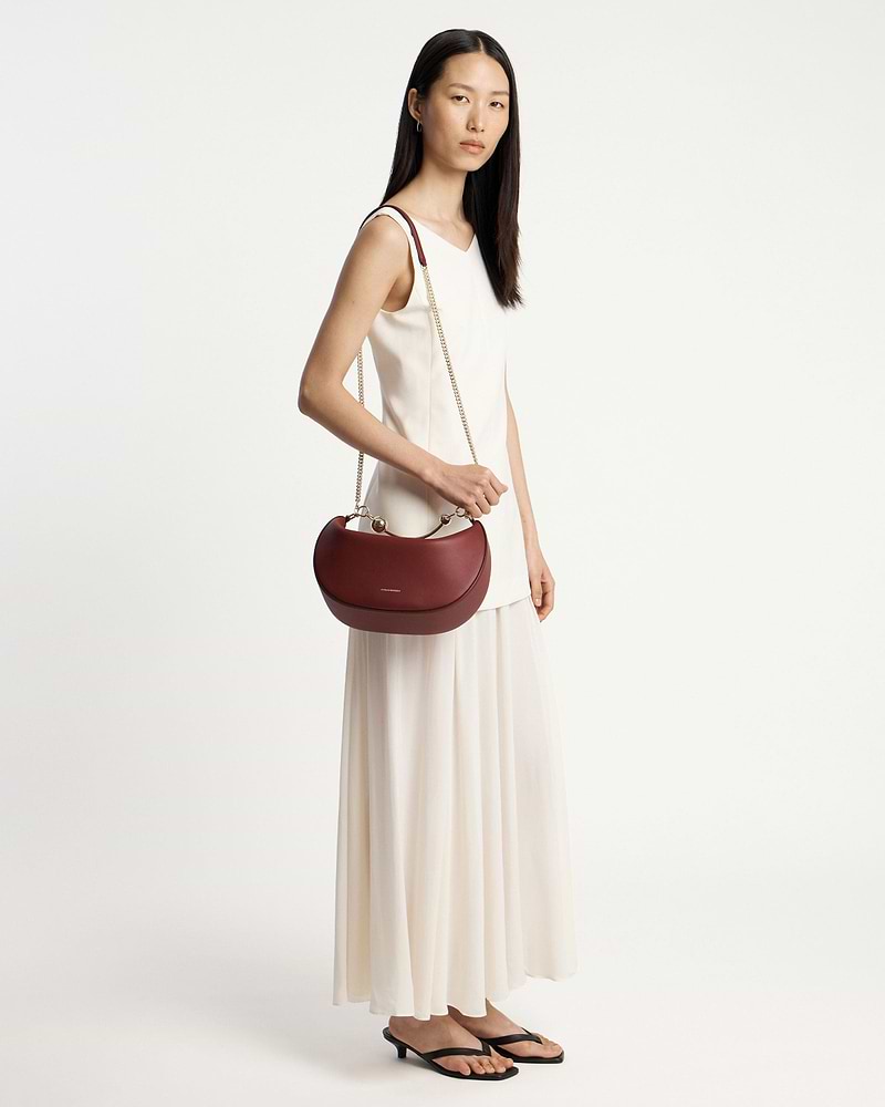 Woman in white dress carrying oxblood crescent moon bag with chain strap