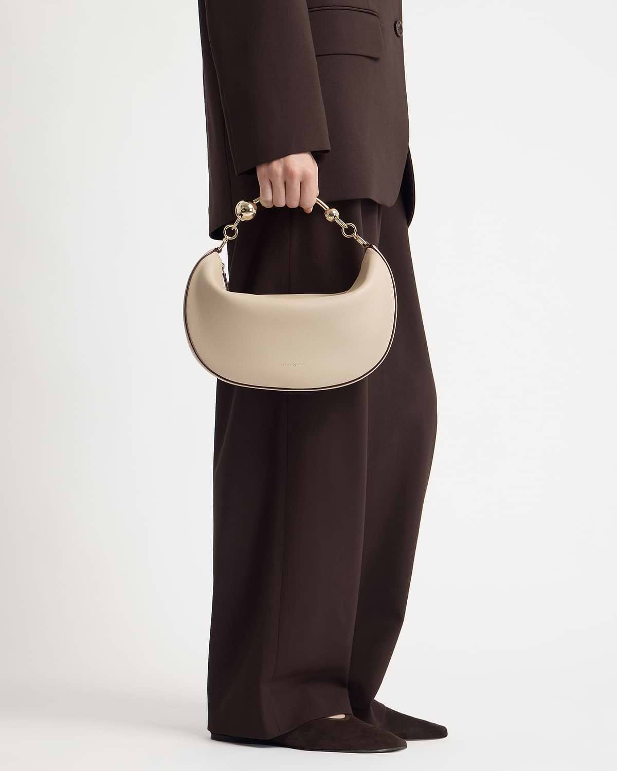 Model holding oat-coloured crescent bag with short gold link handle at side