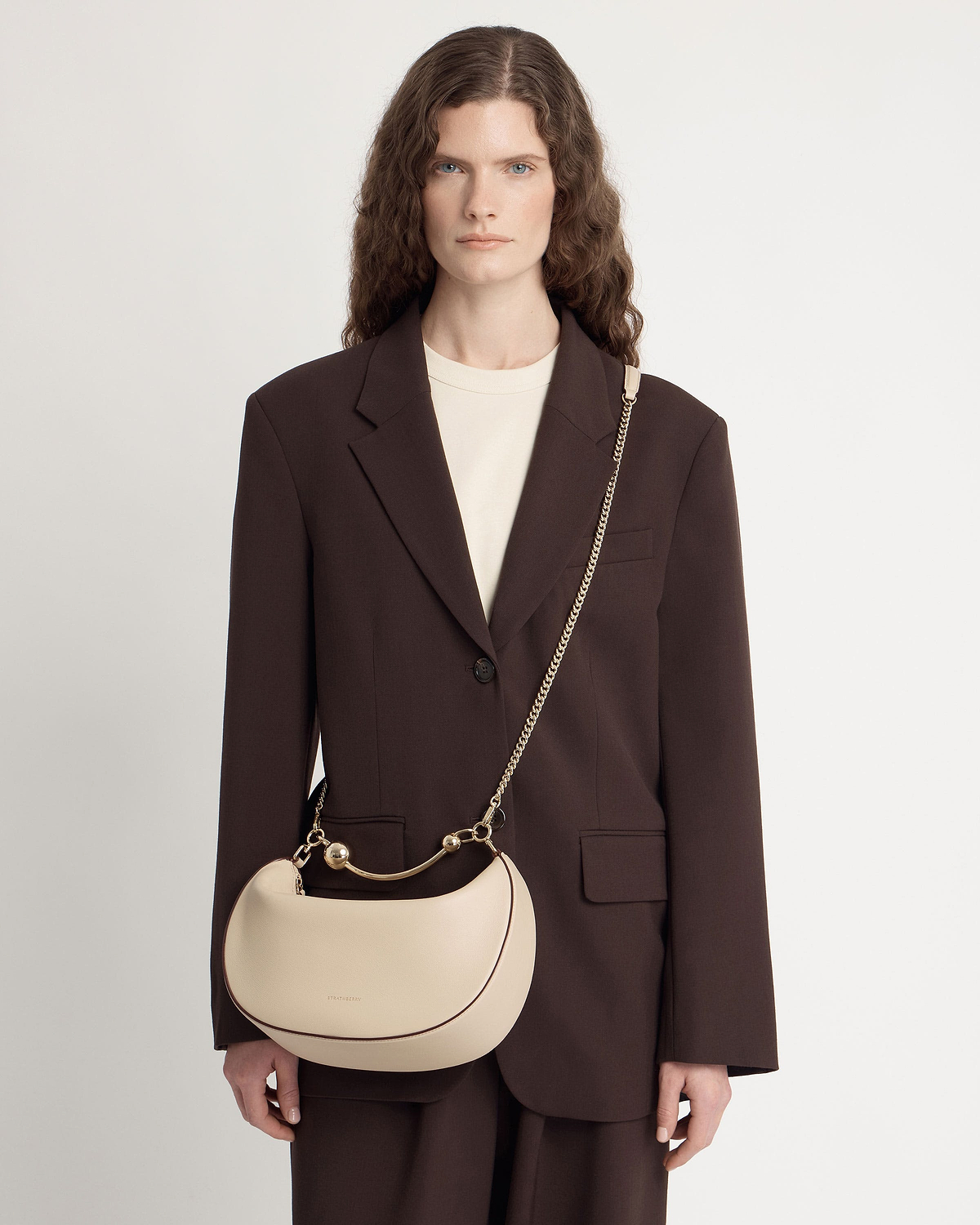 Model wearing oat crescent moon bag with gold chain strap and handle.