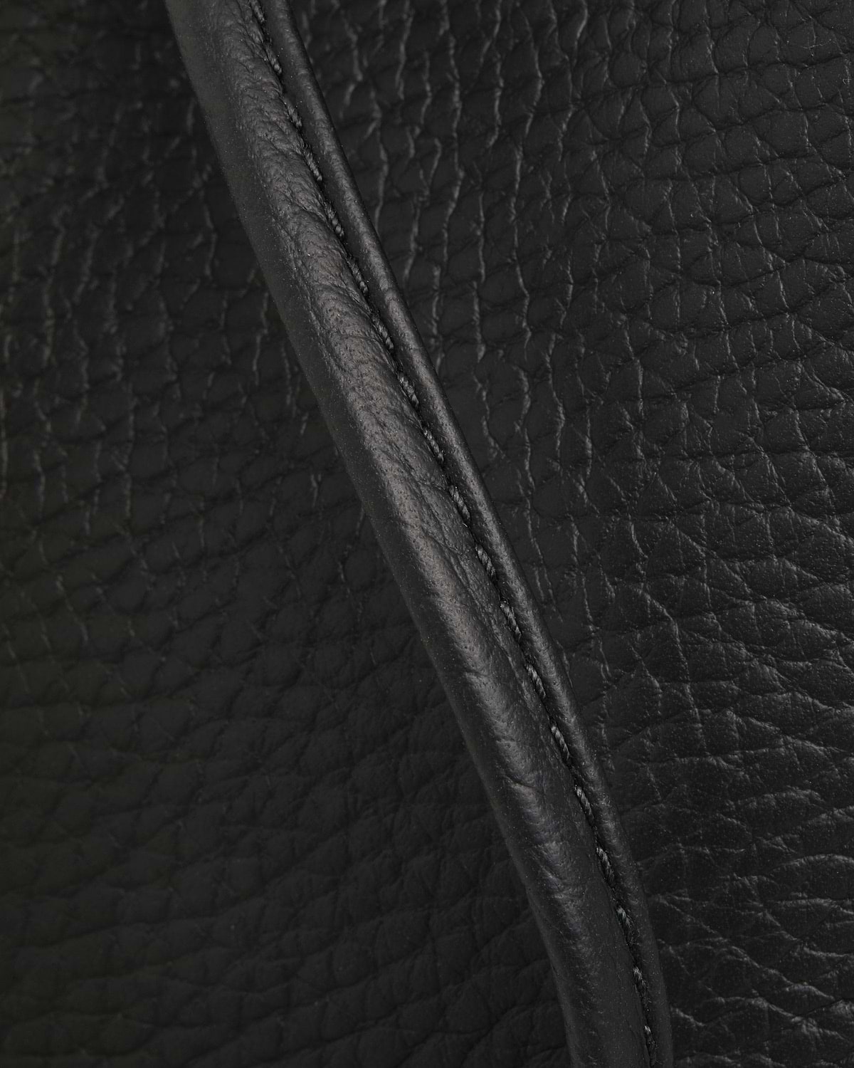 Black pebbled leather with stitched piping, folded edge and visible grain texture.