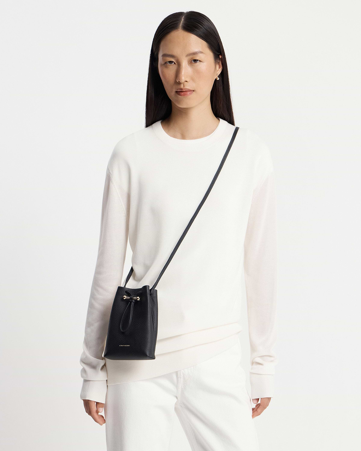 Model wearing a black Strathberry Osette midi pouch crossbody over white jumper.