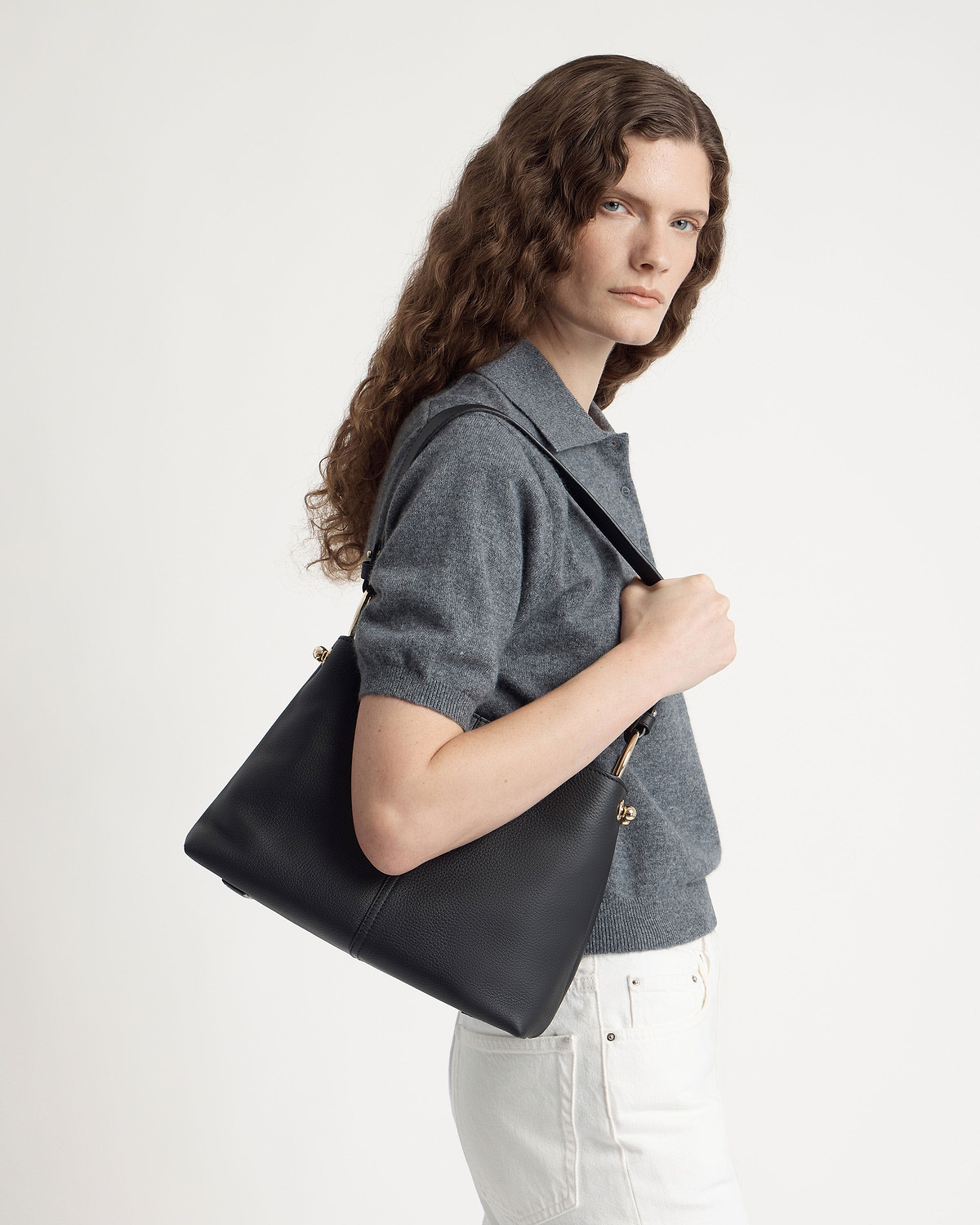 Model wearing grey top carrying black hobo bag over her shoulder.