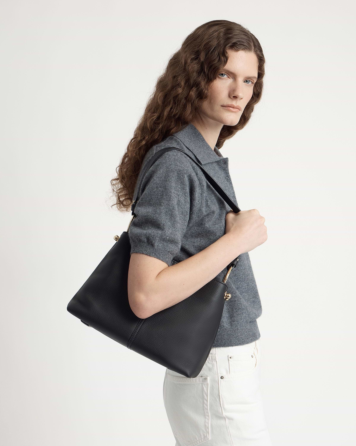 Model wearing grey top carrying black hobo bag over her shoulder.