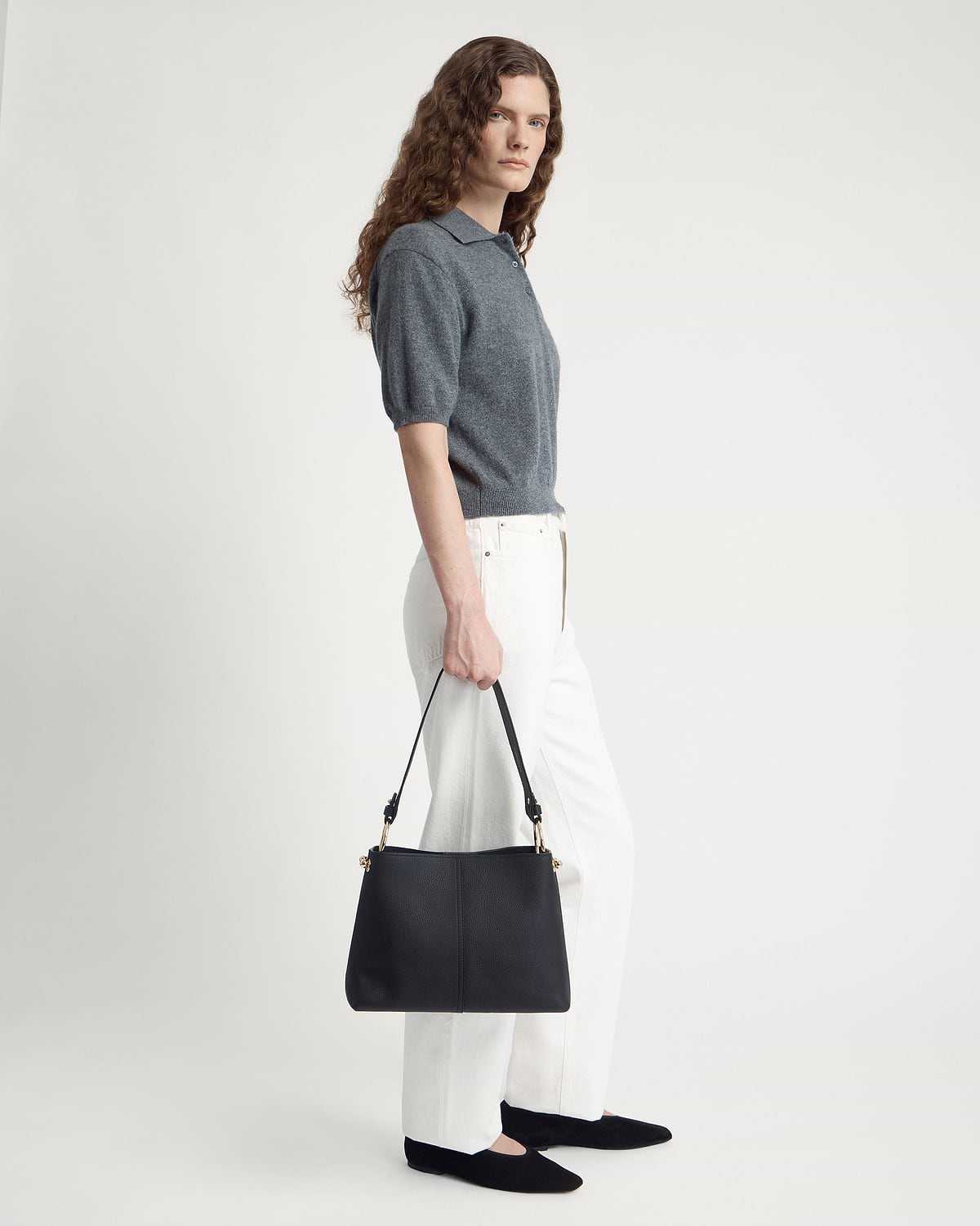 Model holding black hobo bag with single strap and gold hardware.