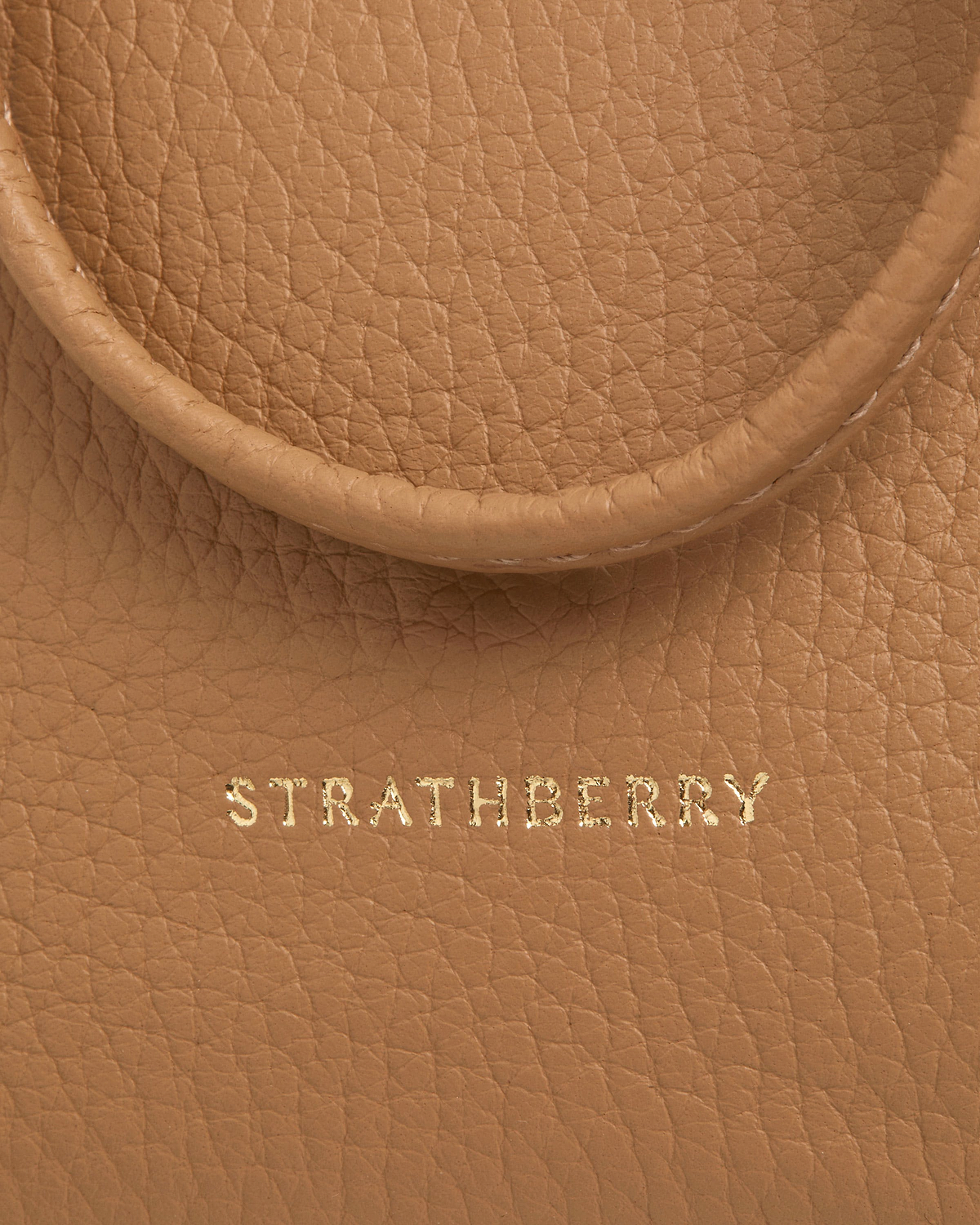 Strathberry logo stamped on caramel pebbled leather midi pouch near handle edge.