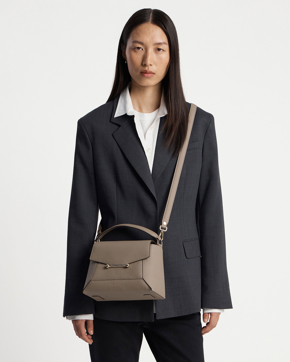 Model wearing dark blazer carrying taupe mosaic bag with top handle and shoulder strap.