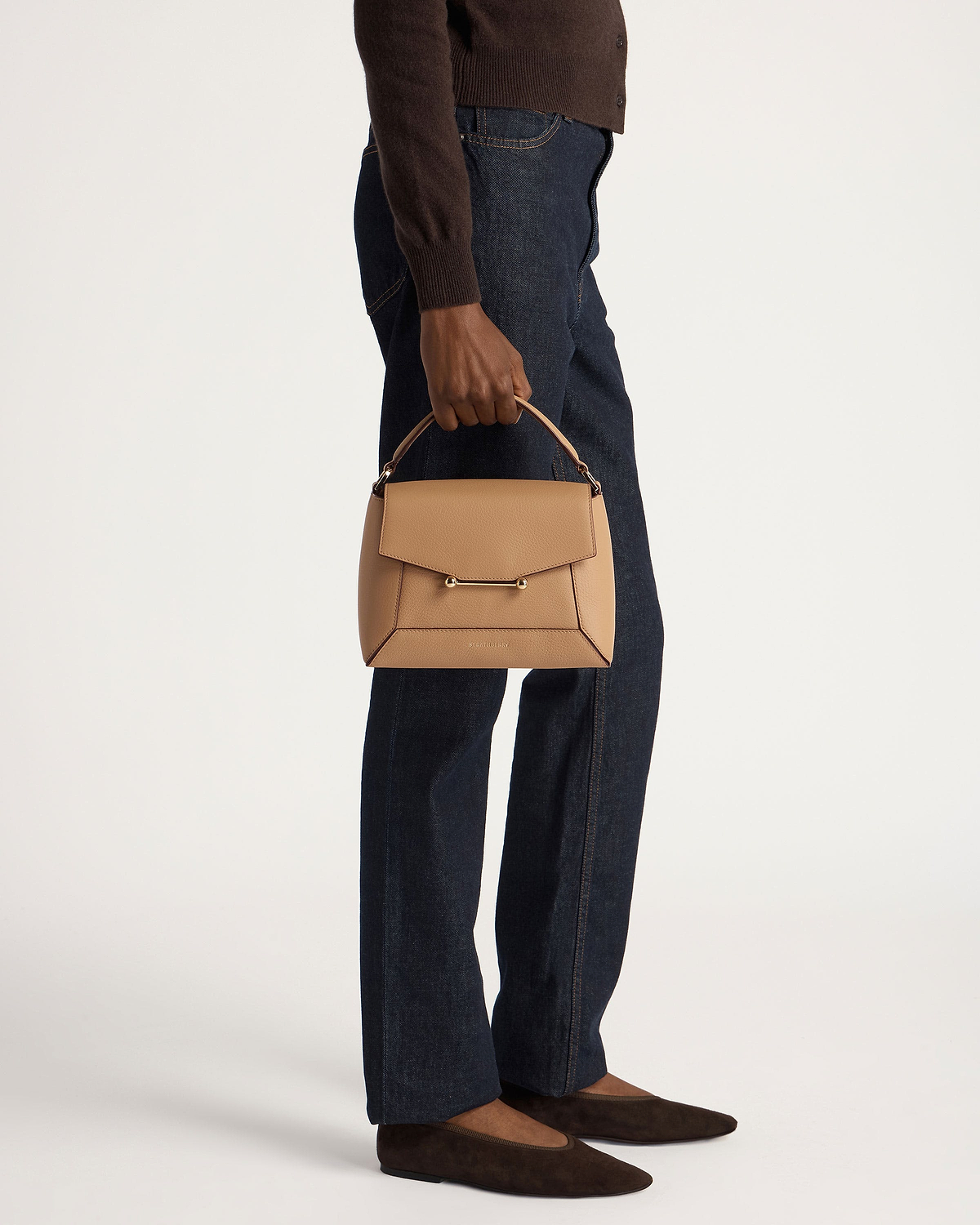 Model holding caramel mosaic bag by the top handle, wearing jeans and brown flats.