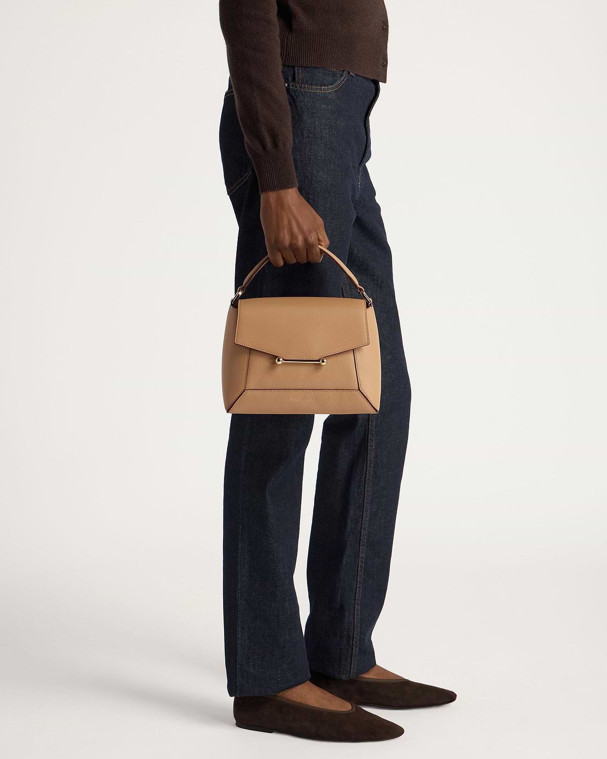 Model holding caramel mosaic bag by the top handle, wearing jeans and brown flats.