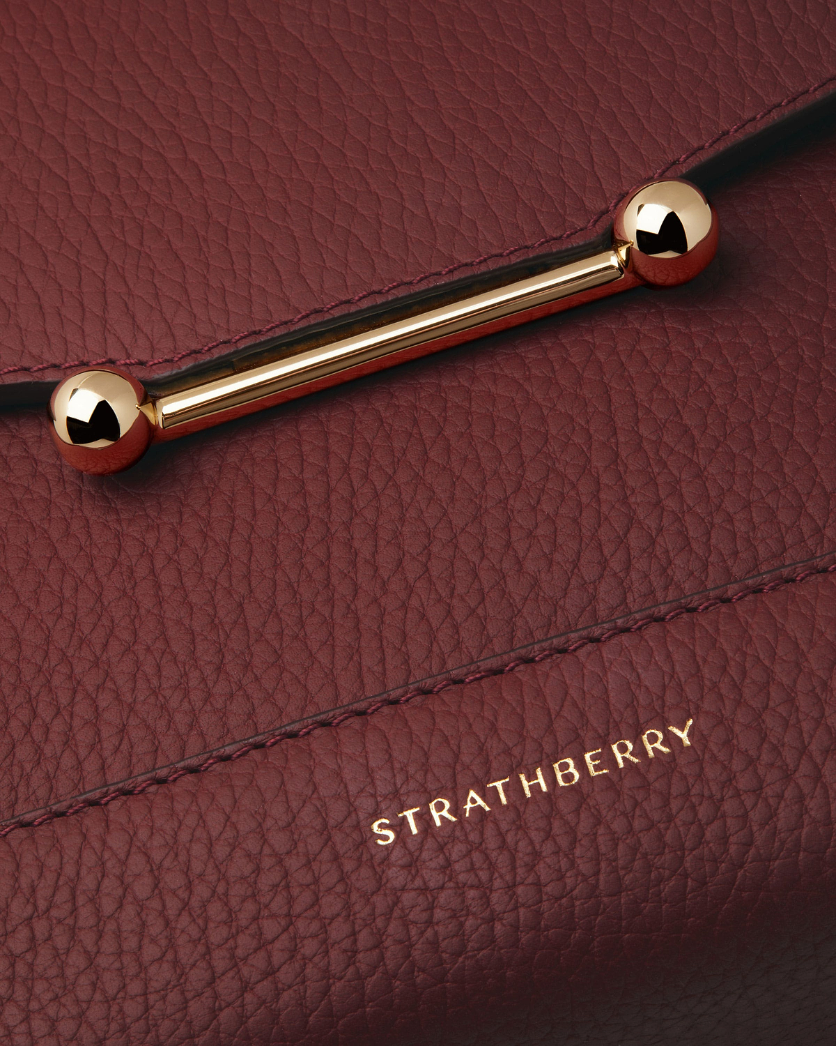Close up of oxblood Strathberry Mosaic bag showing pebbled leather and gold bar.