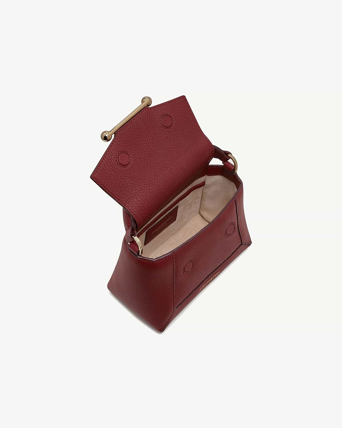 Oxblood leather nano bag open, showing beige suede interior and gold bar