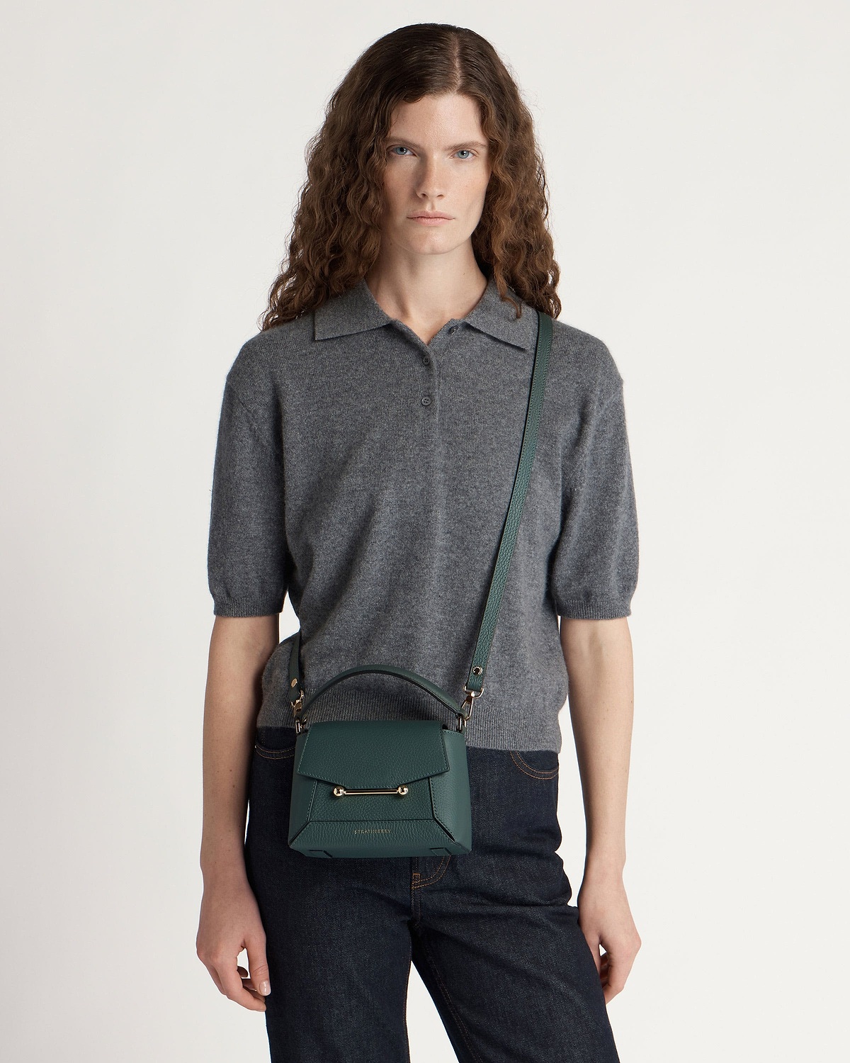 Model wearing bottle green leather crossbody bag with top handle and gold hardware.
