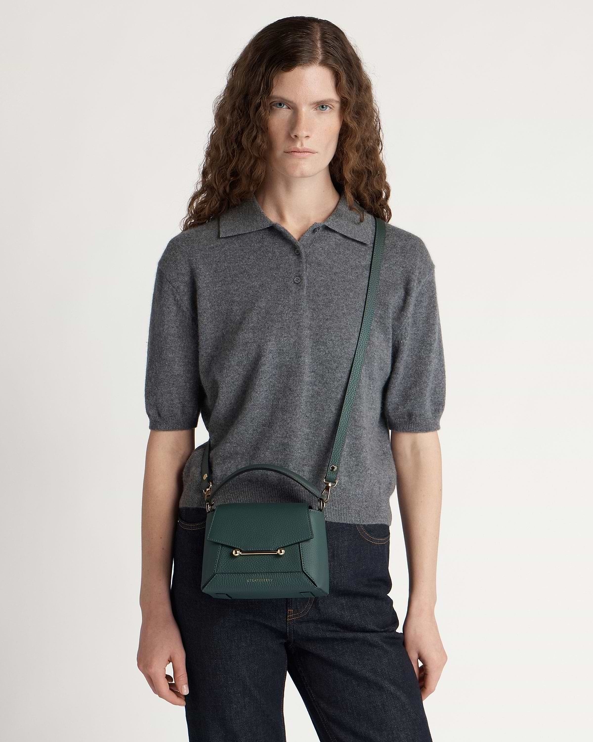 Model wearing bottle green leather crossbody bag with top handle and gold hardware.
