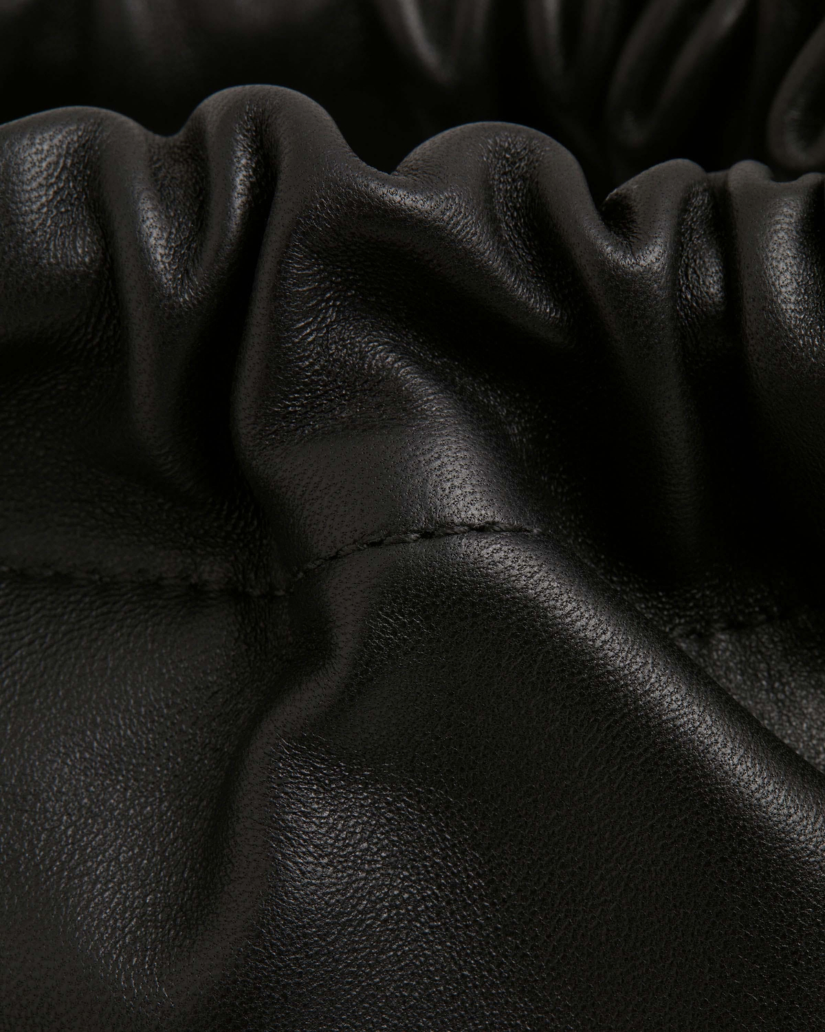 Close-up of black leather drawstring bag with gathered folds and visible stitching