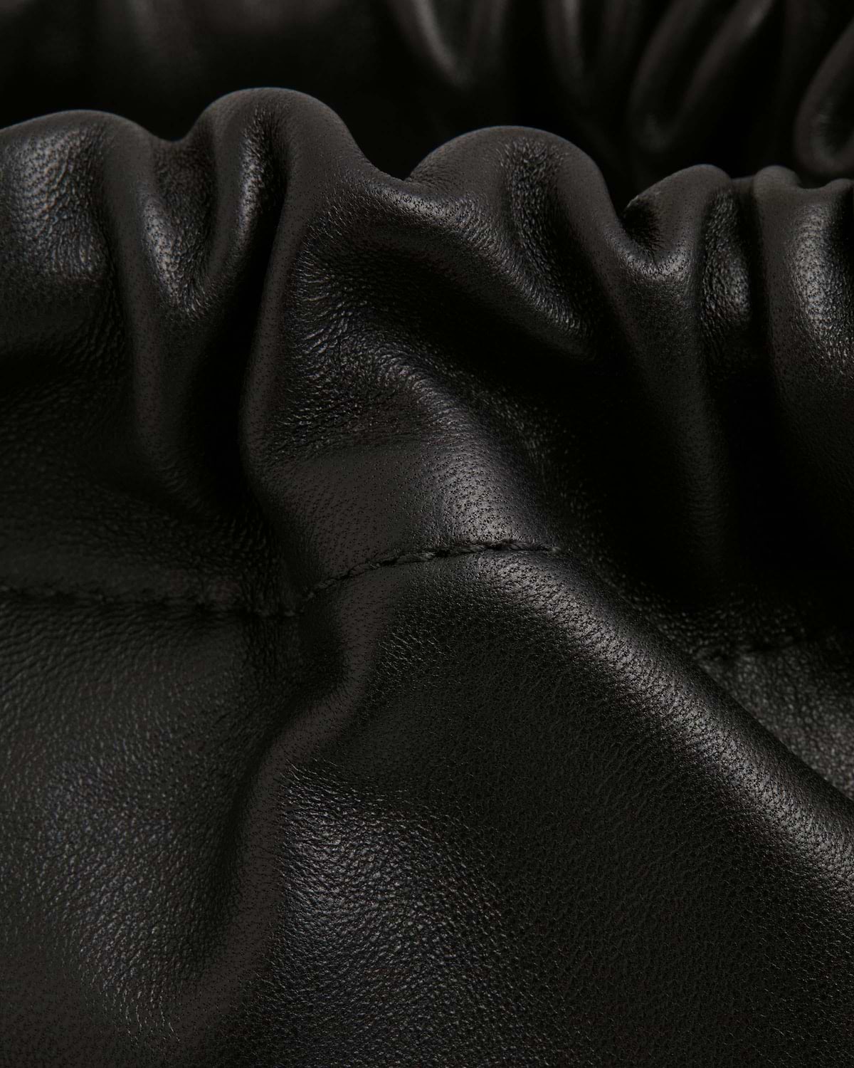 Close-up of black leather drawstring bag with gathered folds and visible stitching