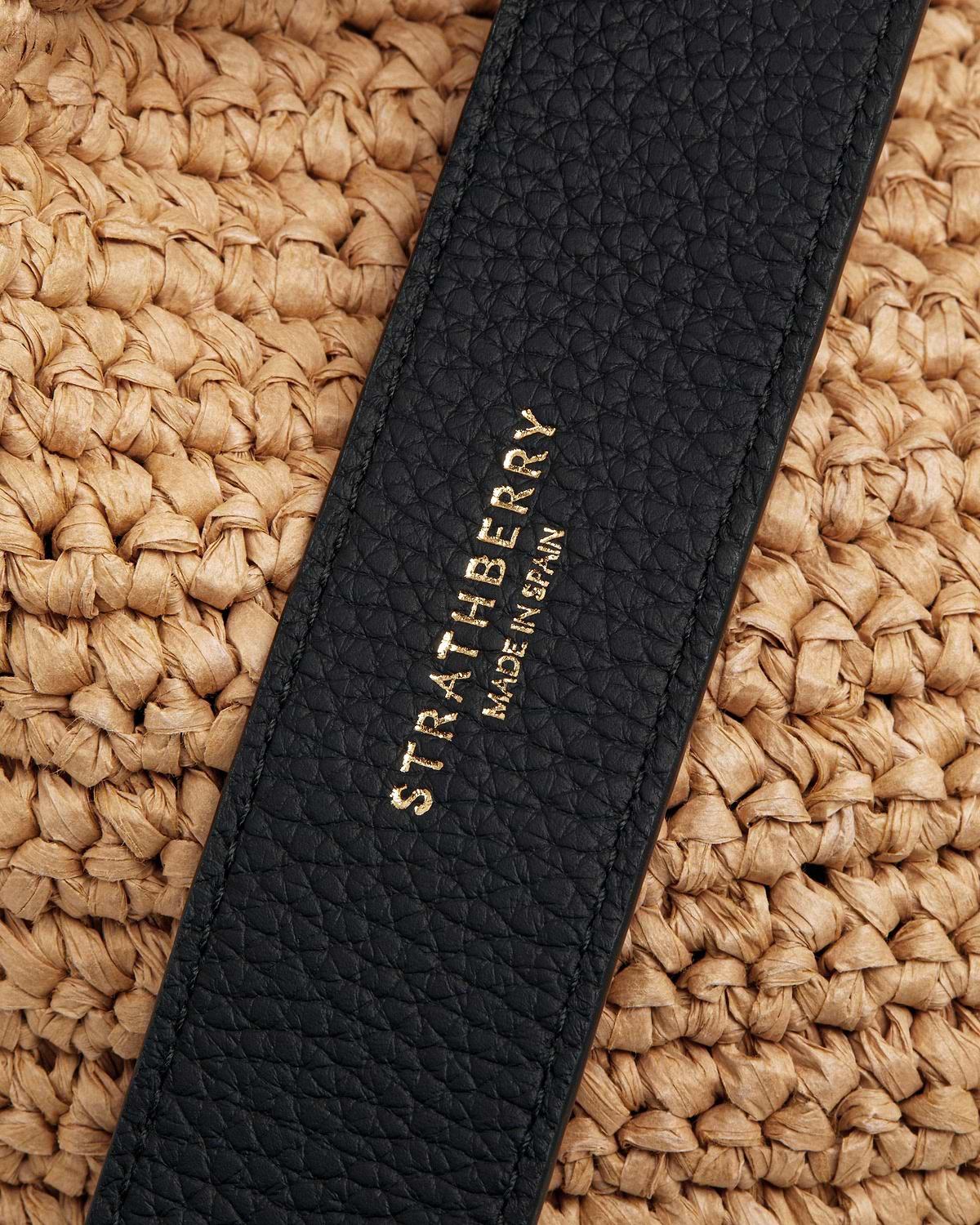 Black pebbled leather strap with gold Strathberry logo on raffia weave.