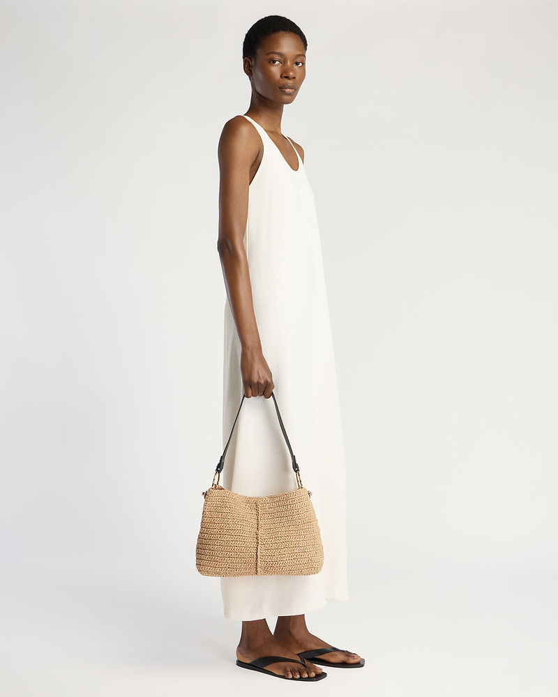 Model in white sleeveless dress holding raffia hobo bag with black strap