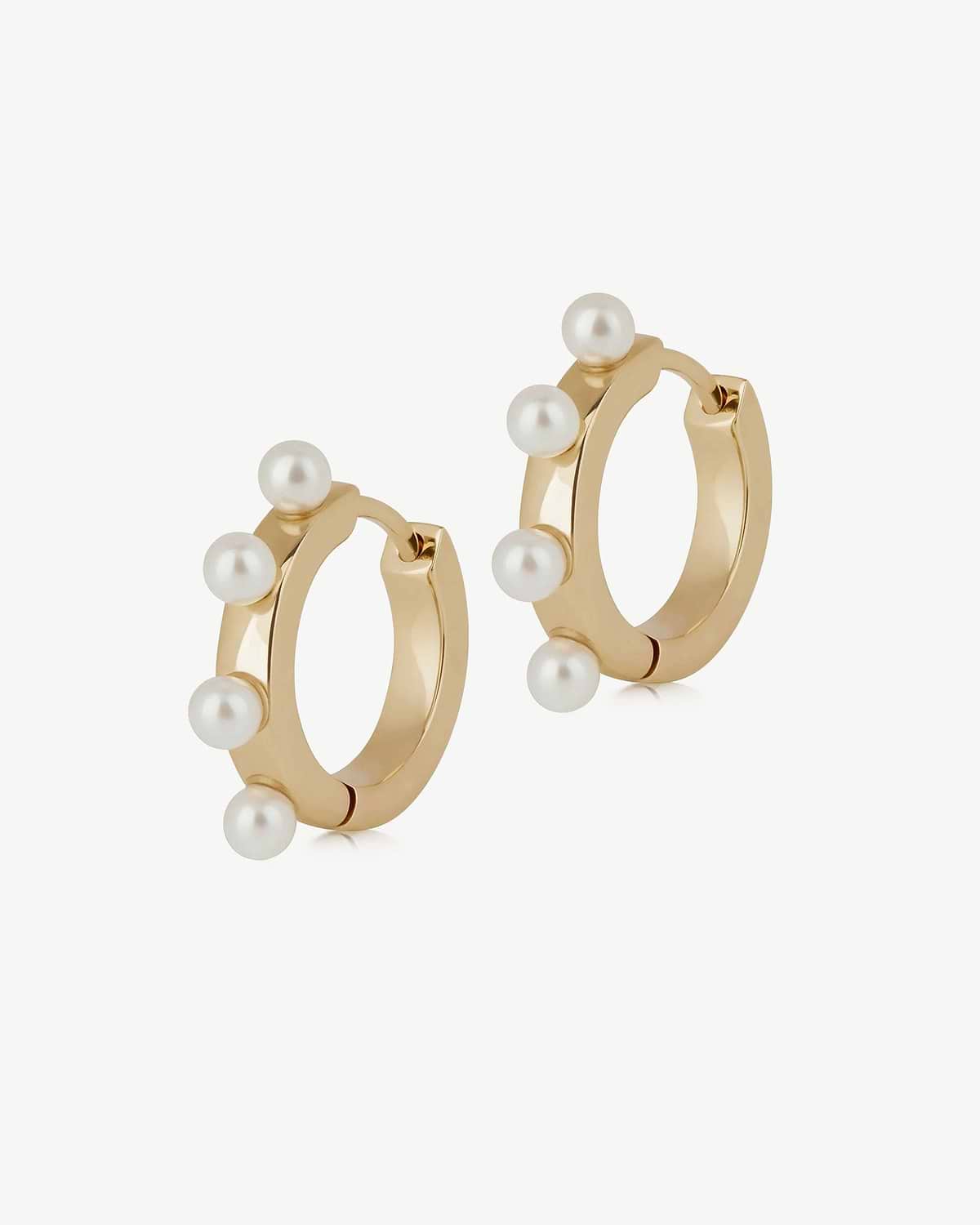 Pair of small gold huggie earrings, each set with four white pearls.