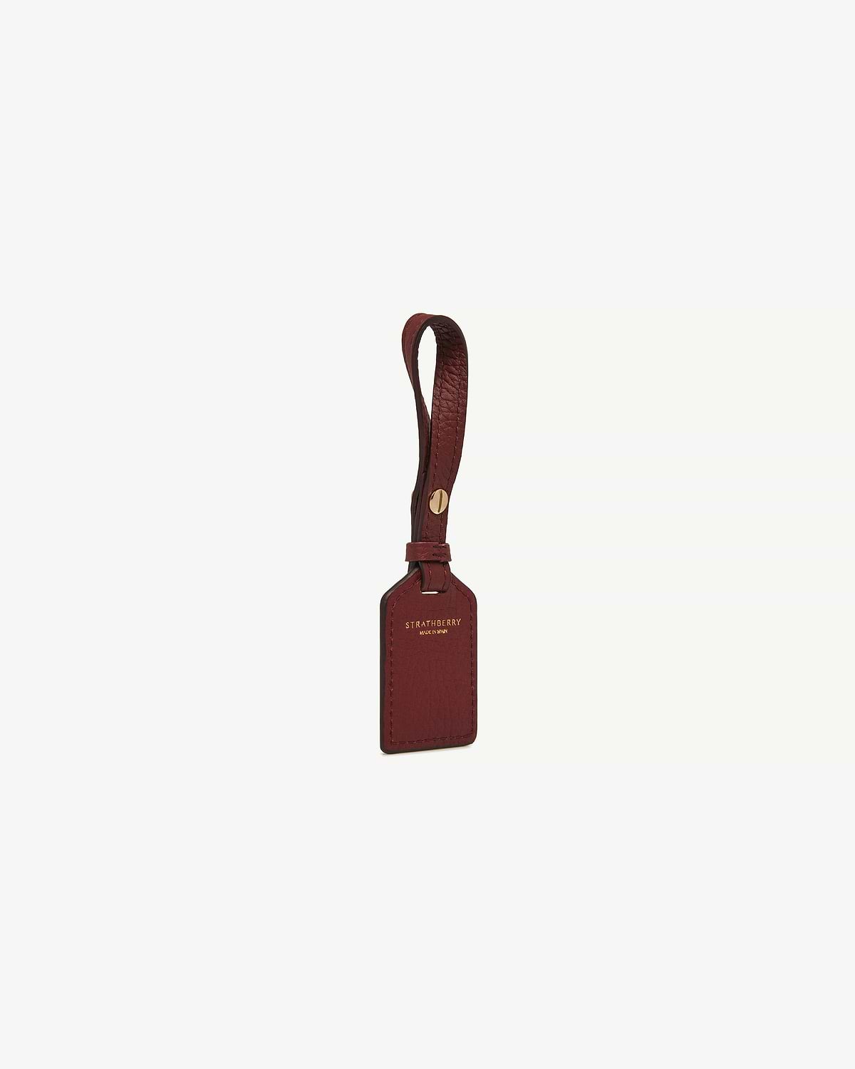 Oxblood leather tag with Strathberry gold logo and leather strap.