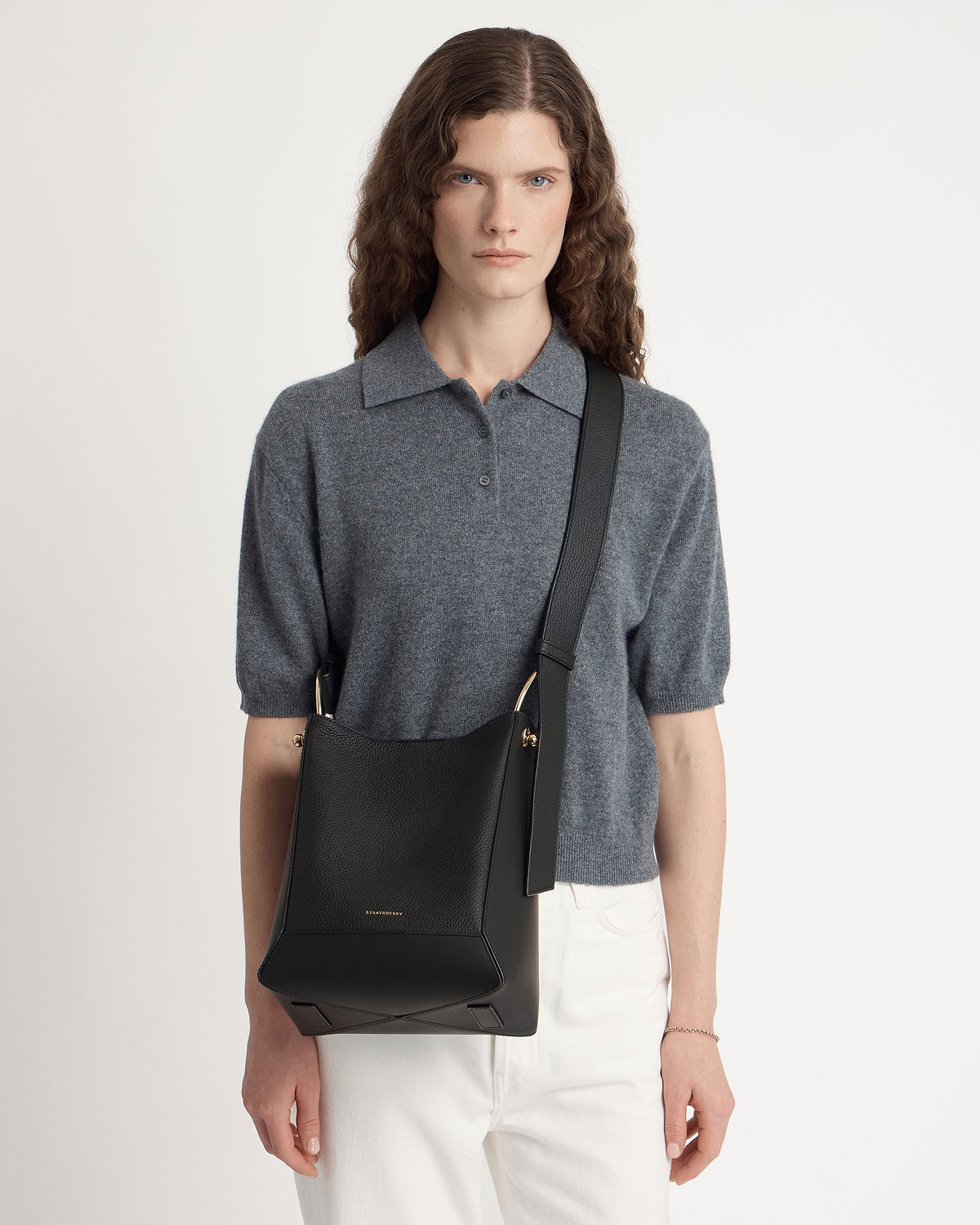 Model wearing black midi bucket bag with wide shoulder strap and gold hardware.
